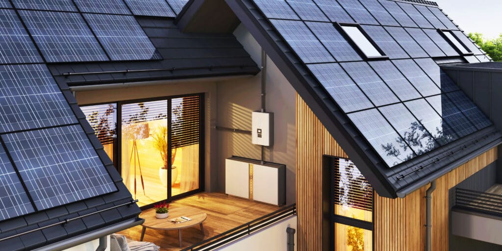 Maison moderne avec toit noir couvert de panneaux solaires bleus, balcon en bois et unité de gestion énergétique murale.