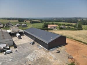 Ouvriers installent un filet de sécurité sur le toit bleu foncé d'un hangar agricole neuf, vue aérienne campagne.