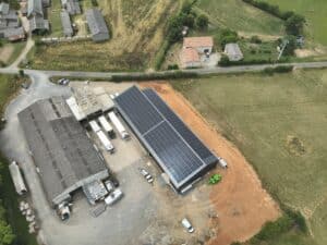 Vue aérienne d'un complexe industriel avec un entrepôt au toit gris et un nouveau bâtiment solaire. Camions de livraison stationnés.
